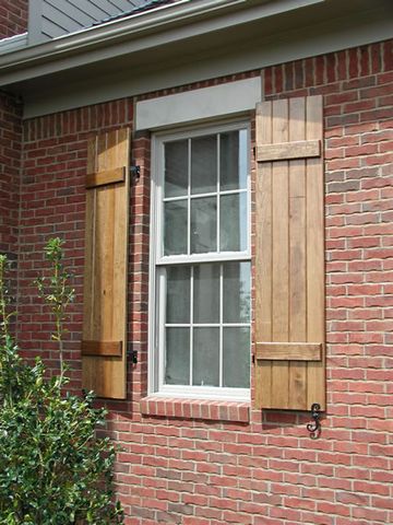 Natural stain-grade closed board and batten shutters on red brick, with shutter dogs.
