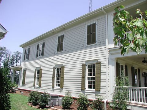 White two-story with olive louvered shutters and a wrap-around porch, side elevation.
