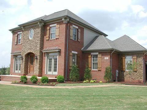 Brick and stone home with natural board and batten shutters and a stone entry tower.