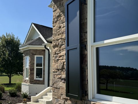 Black composite flat panel shutter on a stone home, angled view of the two-panel design.