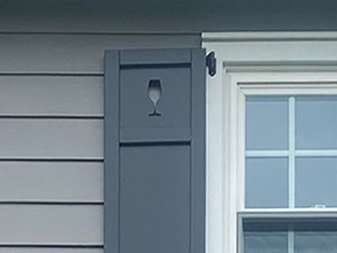 Charcoal composite flat panel shutter with a wine glass cutout on gray lap siding, with an S-scroll shutter dog.