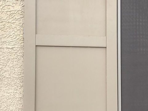 Taupe composite flat panel shutter on a stucco wall, two-panel design with a center rail.
