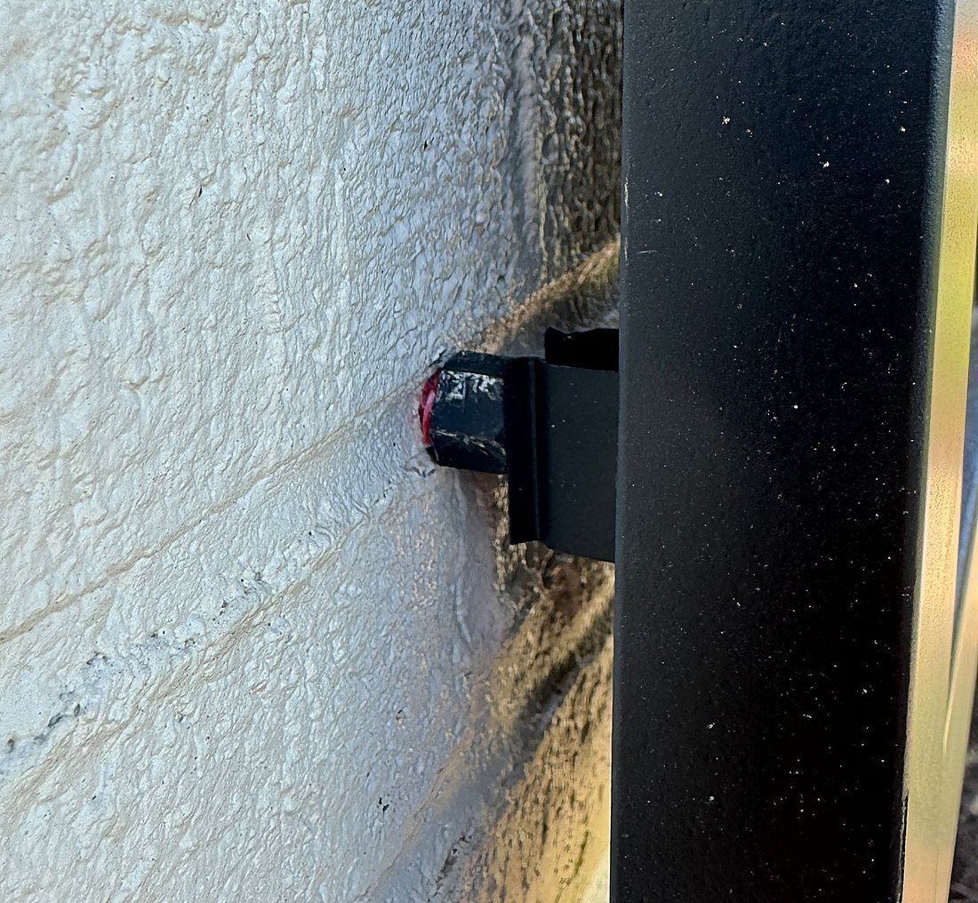 Black bullet catch on a shutter edge closing over the bullet screwed into a painted block wall