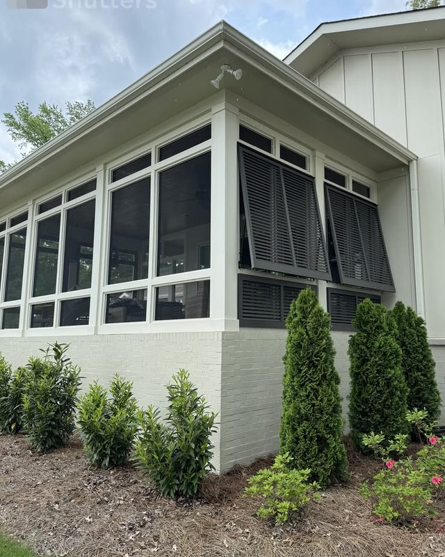 Black Bahama shutters shading a screened porch on a white home