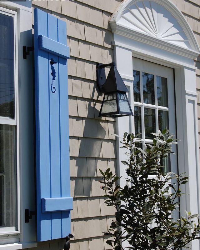 Blue custom board and batten shutter with a seahorse cutout on a cedar shingle coastal home