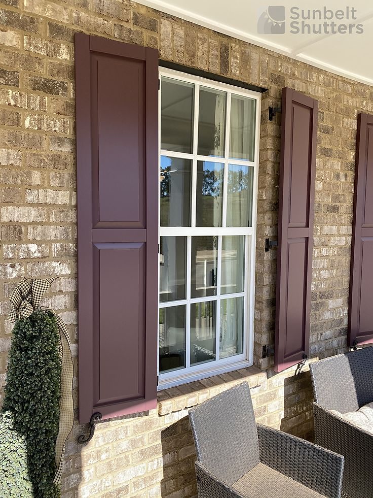 Burgundy raised panel shutters on tan brick