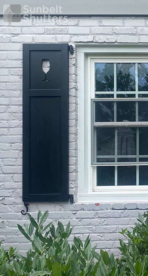 Wine glass cut-out in a black raised panel shutter on white brick